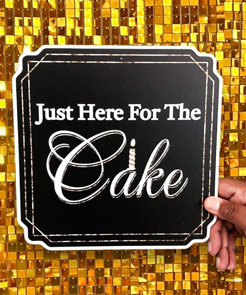 A person holding a photo booth prop that reads “Just Here for the Cake.”